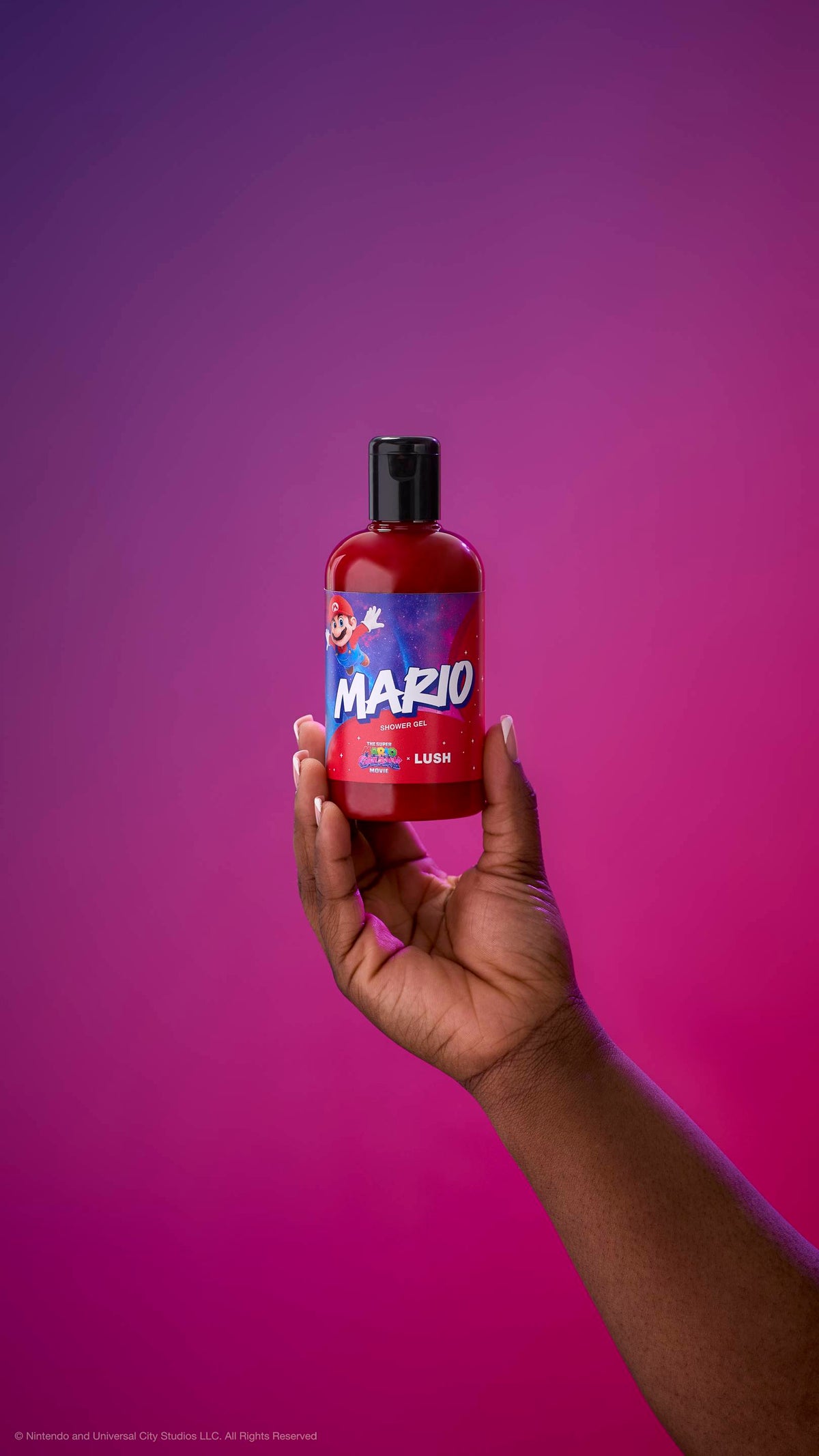 Hand holds a red Mario shower gel bottle with a black cap against a purple-magenta gradient background. The label features Mario jumping against a starry galaxy background with "MARIO SHOWER GEL" in bold letters.